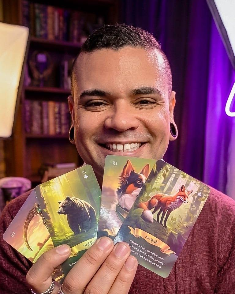 Felipe Araujo sorrindo e mostrando quatro cartas de oráculo com ilustrações de animais